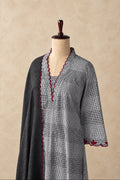 A gray and white checkered tunic with red scalloped trim, displayed on a mannequin against a textured beige wall.