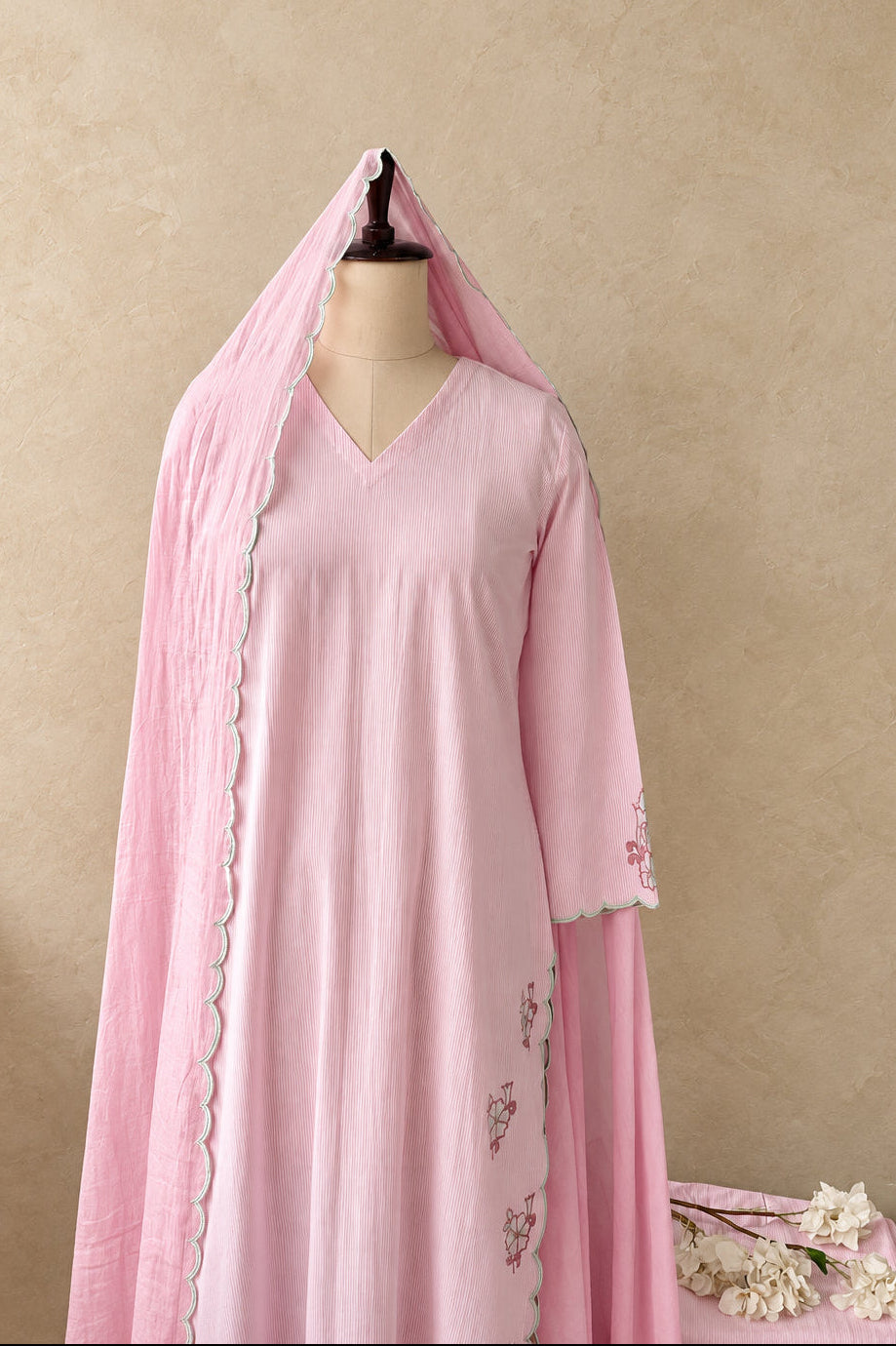 A light pink traditional tunic dress displayed on a mannequin, featuring a matching sheer pink dupatta draped over the shoulders with scalloped edges and subtle floral embroidery on the sleeve.